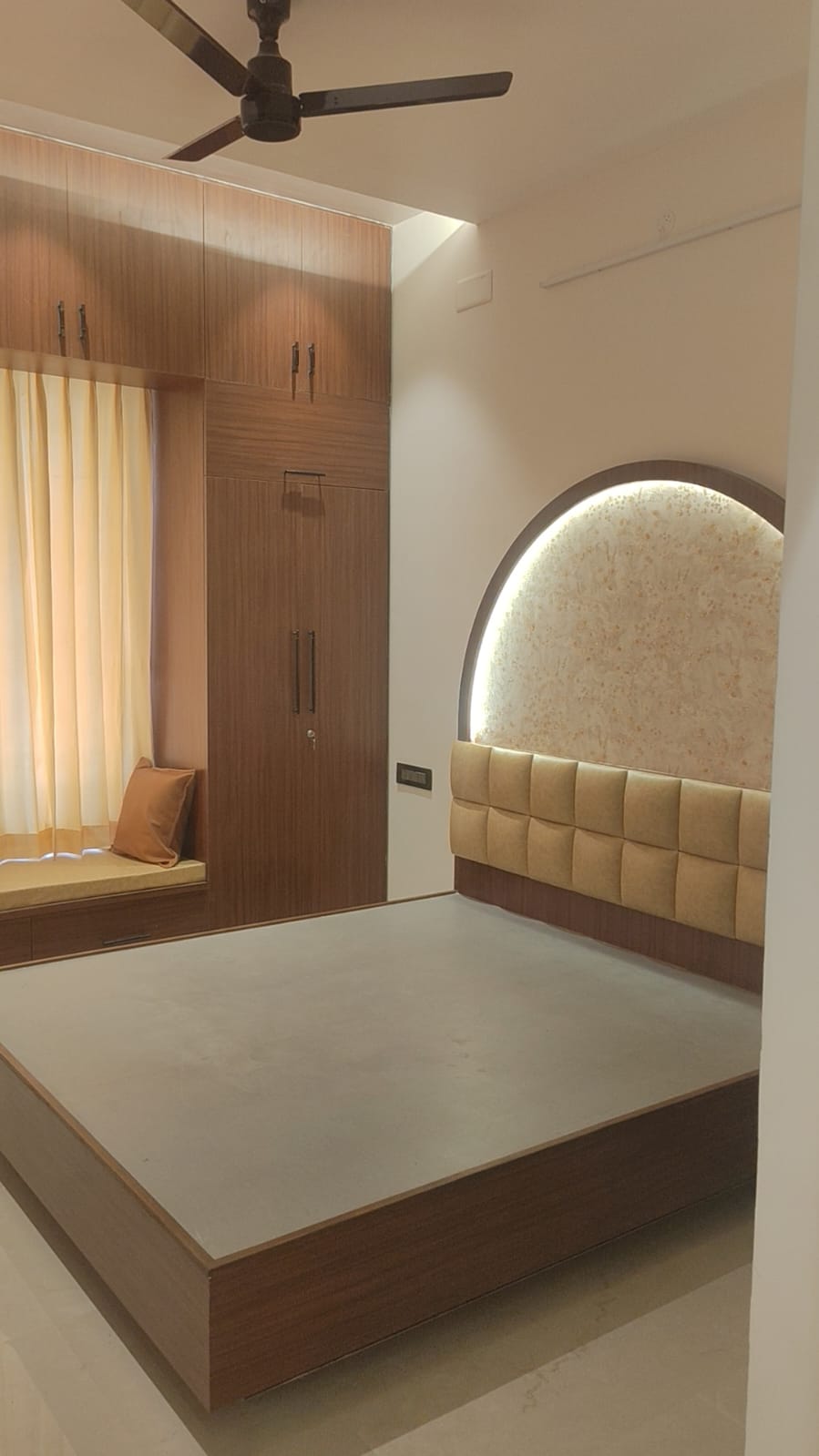 Master bedroom interior Coimbatore – backlit headboard feature wall and floor-to-ceiling wood wardrobe